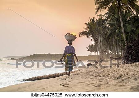 Stock Photography - Local woman carrying goods on her head, beach, sunset, Volta River, Ghana, Africa. Fotosearch