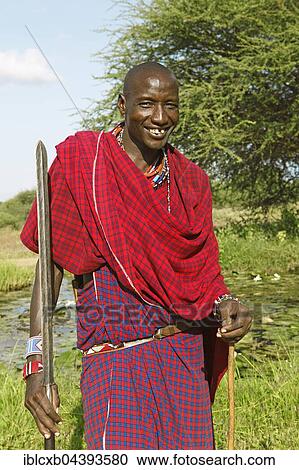 Stock Image - Male Maasai in traditional Shuka clothing with spear, Tsavo West National Park, Taita-Taveta County, Kenya, Africa. Fotosearch