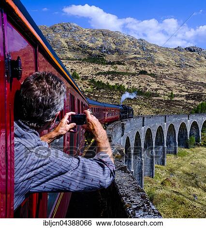Man leans out the window taking a picture of historic train "The Jacobite" Steam Train driving over the Glenfinnan Viaduct, Glenfinnan, Highland, Scotland, United Kingdom, Europe View Large Photo Image Stock Photograph - Man leans out the window taking a picture of historic train "The Jacobite" Steam Train driving over the Glenfinnan Viaduct, Glenfinnan, Highland, Scotland, United Kingdom, Europe. Fotosearch