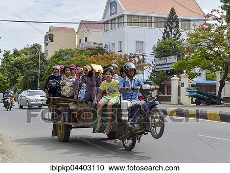 Stock Image - Man on scooter makes a wheelie, trailer loaded with many people, Phnom Penh, Cambodia, Asia. Fotosearch