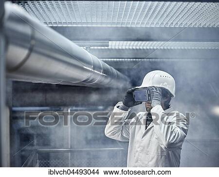 Man with VR goggles, white helmet and lab coat standing in front of industrial plant, Austria, Europe View Large Photo Image Picture - Man with VR goggles, white helmet and lab coat standing in front of industrial plant, Austria, Europe. Fotosearch
