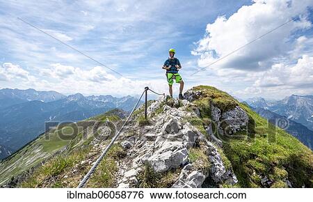 Stock Photograph - Mountaineer on a ridge on a secured fixed rope route, Mittenwalder Höhenweg, view of mountain panorama, Karwendel Mountains, Mittenwald, Bavaria, Germany, Europe. Fotosearch