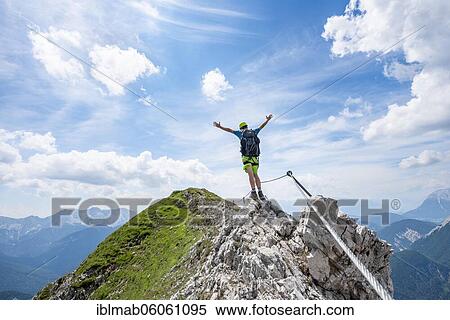 Stock Photography - Mountaineer on a ridge on a secured fixed rope route, stretching his arms in the air, Mittenwalder Höhenweg, view of mountain panorama, Karwendel Mountains, Mittenwald, Bavaria, Germany, Europe. Fotosearch