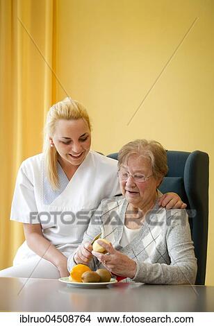 Picture - Nurse helping a senior citizen to peel fruit, Germany, Europe. Fotosearch