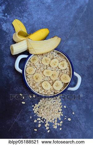 Stock Image - Oat flakes in bowl with banana slices, Avena sativa, muesli. Fotosearch