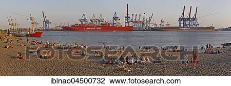 Stock Image - People having a picnic, Elbstrand in front of container port Hamburg Süd, evening mood, at Övelgönne, Hamburg, Germany, Europe. Fotosearch