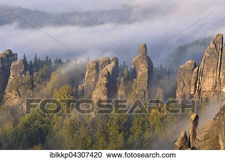 Stock Image - Rock serrated crown, Viererturm and Schramm gatekeepers in morning mist, Autumn, Elbe Sandstone Mountains, Saxon Switzerland, Saxony, Germany, Europe. Fotosearch
