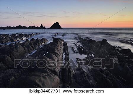 Stock Image - Rocks in the sea, rocky coast in the evening light, Atlantic Coast, Hartland Quay, Devon, United Kingdom, Europe. Fotosearch