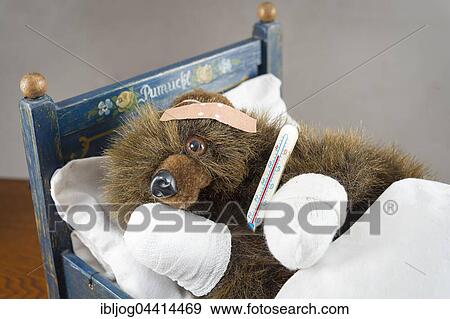 Stock Photo - Sick Teddy bandaged paws and head, holding thermometer, in an original Pumuckl crib. Fotosearch