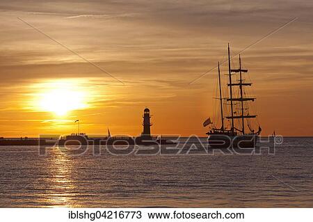 Stock Image - Sunset at harbor entrance, backlit sailboat, Hanse-Sail, Rostock, Mecklenburg-Western Pomerania, Germany, Europe. Fotosearch
