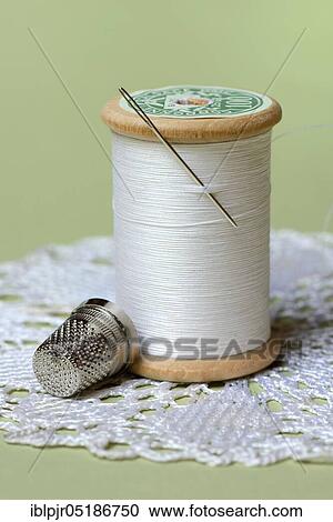Stock Image - Thread roll with sewing needle and thimble. Fotosearch