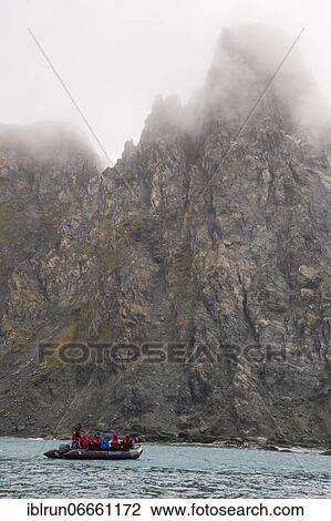 Stock Image - Tourists on a zodiac before the rugged coastline of Elephant island, South Shetland islands, Antarctica. Fotosearch