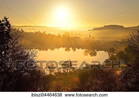 Town with church near lake, Schalkenmehrener Maar in autumn at sunrise, water reflection, Schalkenmehren, Daun, Vulkaneifel, Eifel, Rhineland-Palatinate, Germany, Europe View Large Photo Image Stock Photo - Town with church near lake, Schalkenmehrener Maar in autumn at sunrise, water reflection, Schalkenmehren, Daun, Vulkaneifel, Eifel, Rhineland-Palatinate, Germany, Europe. Fotosearch