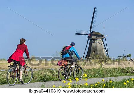 Stock Photo - Two cyclists passing a windmill in Kinderdijk, The Netherlands, Europe. Fotosearch