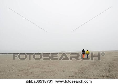 Stock Image - Two people walking on a sandy beach in fog, North Sea, Norderney, Lower Saxony, Germany, Europe. Fotosearch