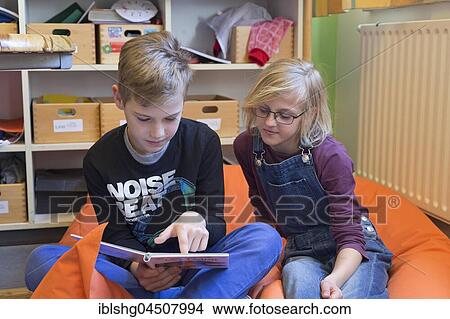 Picture - Two students in elementary school reading a book, sitting on beanbag, Lower Saxony, Germany, Europe. Fotosearch