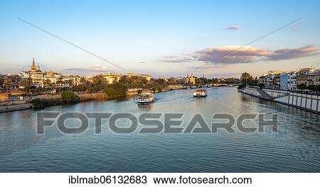 Stock Image - View over the river Rio Guadalquivir with excursion boats, promenade on Calle Betis in Triana and view of Torre del Oro, sunset, Sevilla, Andalusia, Spain, Europe. Fotosearch