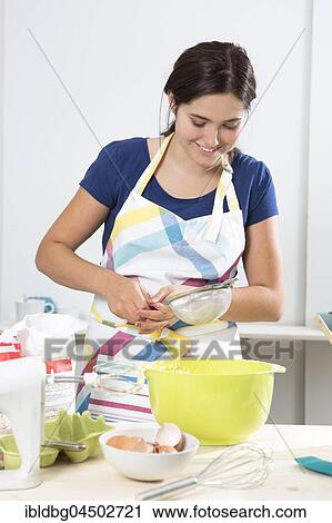 Stock Image - Young woman baking cake, sifting flour, Bavaria, Germany, Europe. Fotosearch