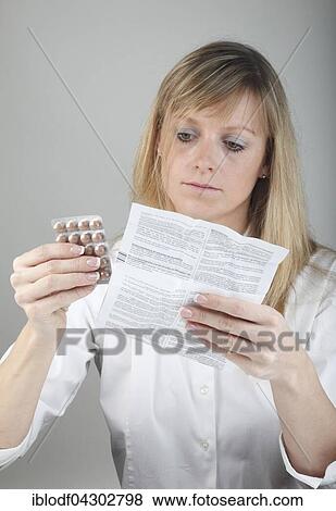 Stock Photo - Young woman reading the package insert of a drug holding tablets in hand. Fotosearch
