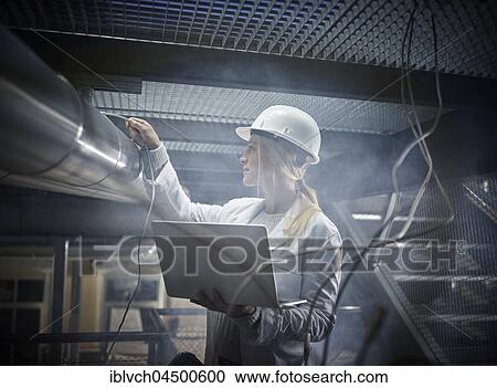 Young woman with helmet, white lab coat and laptop standing in front of an industrial plant, Austria, Europe View Large Photo Image Stock Image - Young woman with helmet, white lab coat and laptop standing in front of an industrial plant, Austria, Europe. Fotosearch