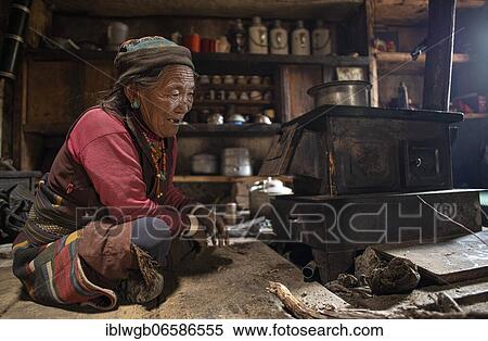 Stock Photography - An elderly woman sitting in front of a small stove in her kitchen, Tsakhang Gompa, Dolpo, Nepal, Asia. Fotosearch