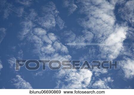 Stock Photo - Commercial airplane with condensation trails in blue cloudy sky, Bern, Switzerland, Europe. Fotosearch