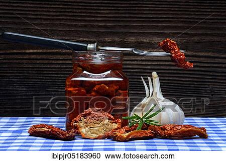 Stock Image - Dried tomatoes in jar with olive oil, antipasti, olive oil, garlic. Fotosearch