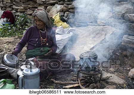 Stock Image - Elderly woman, Tibetan, preparing tea water at a smoking wood fire, Dolpo, Nepal, Asia. Fotosearch