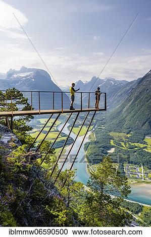 Stock Image - Hikers standing on viewing platform Rampestreken, hiking Romsdalseggen, river Rauma, Romsdalfjellene mountains, Andalsnes, Møre og Romsdal, Norway, Europe. Fotosearch