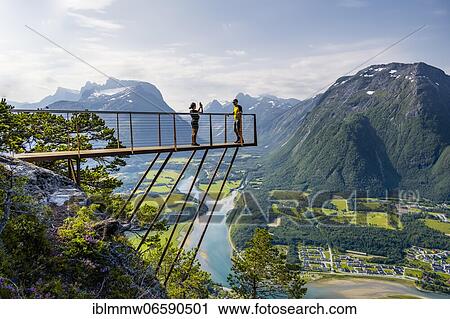 Stock Image - Hikers standing on viewing platform Rampestreken, hiking Romsdalseggen, river Rauma, Romsdalfjellene mountains, Andalsnes, Møre og Romsdal, Norway, Europe. Fotosearch