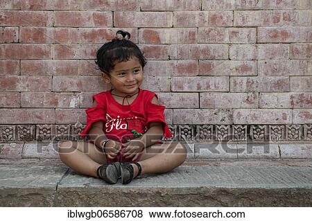 Stock Photo - Little girl sitting in front of a house wall, Patan, Kathmandu Valley, Nepal, Asia. Fotosearch
