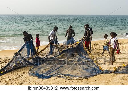 Stock Image - Local fishermen pulling their nets on a beach in Robertsport, Liberia, Africa. Fotosearch