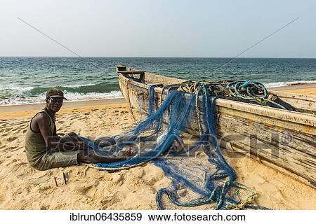 Man fixing his nets in his fishing boats on a beach in Robertsport, Liberia, Africa View Large Photo Image Stock Photo - Man fixing his nets in his fishing boats on a beach in Robertsport, Liberia, Africa. Fotosearch