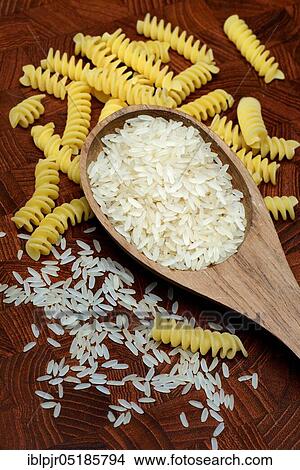 Picture - Rice grains in wooden spoon and spiral noodles, rice grain, rice grains, fusilli, uncooked. Fotosearch