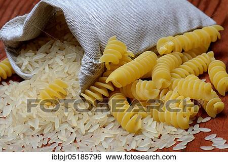 Stock Photograph - Rice grains in wooden spoon and spiral noodles, rice grain, rice grains, fusilli, uncooked. Fotosearch