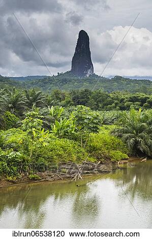 Stock Image - River flowing before the unusal monolith, Pico Cao Grande, east coast of Sao Tome, Sao Tome and Principe, Atlantic Ocean, Africa. Fotosearch
