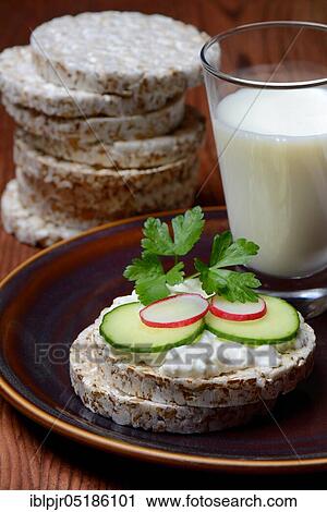 Stock Image - Spelt wafer topped with cream cheese, cucumber and radish, glass of milk, spelt wafers. Fotosearch