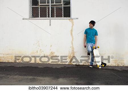 Teenager with his longboard, leaning against a wall View Large Photo Image Picture - Teenager with his longboard, leaning against a wall. Fotosearch