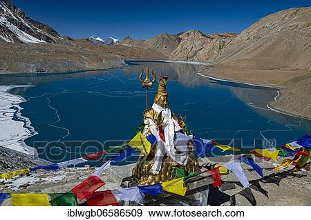 Stock Photo - Tilicho Lake covered with ice in front of mountain scenery with Buddhist prayer flags and Hindu Shiva statue, often called the highest lake in the world, Annapurna region, 4919 m altitude, Himalaya, Nepal, Asia. Fotosearch