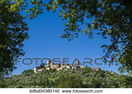 Stock Image - View of a town on a hill, seen through the branches of a tree, Montemerano, Tuscany, Italy, Europe. Fotosearch