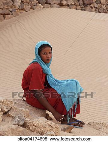 Stock Photo - Young woman in colourful clothes sitting on stone, oasis of Al-Ghazali, Sudan, Africa. Fotosearch