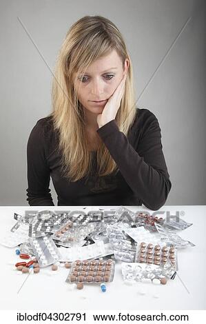 Stock Image - Young woman sitting skeptical, in front of many tablets, drug abuse. Fotosearch