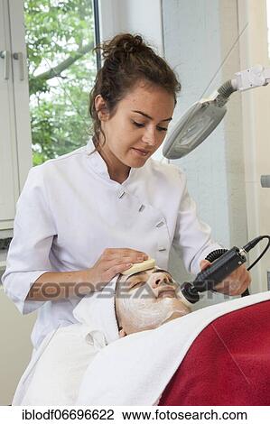Stock Image - Application of the white face pack with moisture and vitamins in connection with the brush grinder for peeling the skin in practical lessons. Training as a beautician at the vocational school, Düsseldorf, North Rhine-Westphalia, Germany, Europe. Fotosearch
