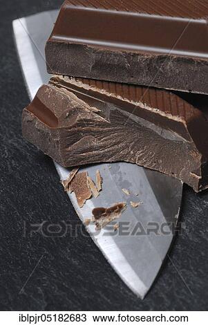 Stock Image - Block chocolate in pieces, chocolate, milk chocolate, milk chocolate, cake glaze, couverture, knife. Fotosearch