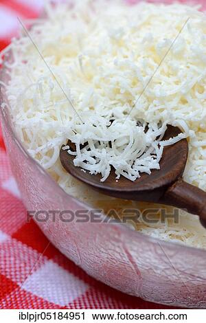 Stock Image - Grated Parmesan cheese in glass bowl with wooden spoon, Parmigiano Reggiano. Fotosearch