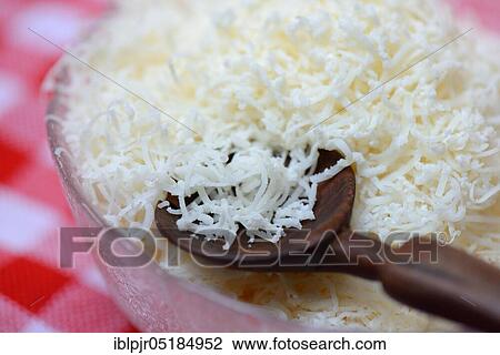 Stock Image - Grated Parmesan cheese in glass bowl with wooden spoon, Parmigiano Reggiano. Fotosearch