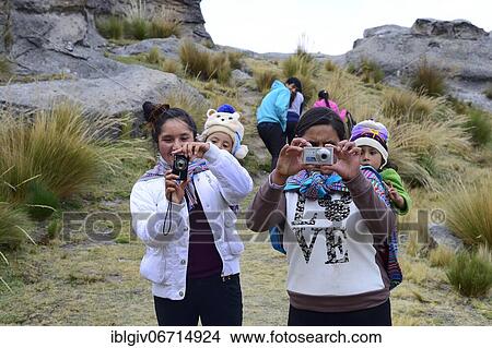 Picture - Indigenous woman with infants on their backs photographing the photographer, Junín Province, Peru, South America. Fotosearch