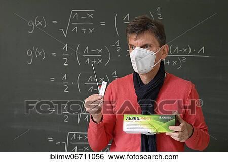 Stock Photograph - Teacher shows Corona antigen rapid test, in front of blackboard, face-to-face teaching, Corona crisis, Germany, Europe. Fotosearch
