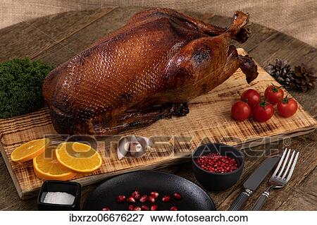 Crispy, roast goose on wooden board with vegetables and cutlery placed around View Large Photo Image Stock Photo - Crispy, roast goose on wooden board with vegetables and cutlery placed around. Fotosearch