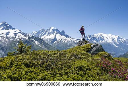 Stock Photograph - Hiker standing on rocks, mountain panorama from Aiguillette des Posettes, left summit of Aiguille Verte (right) Aiguille du Midi and Mont Blanc, Chamonix, Haute-Savoie, France, Europe. Fotosearch